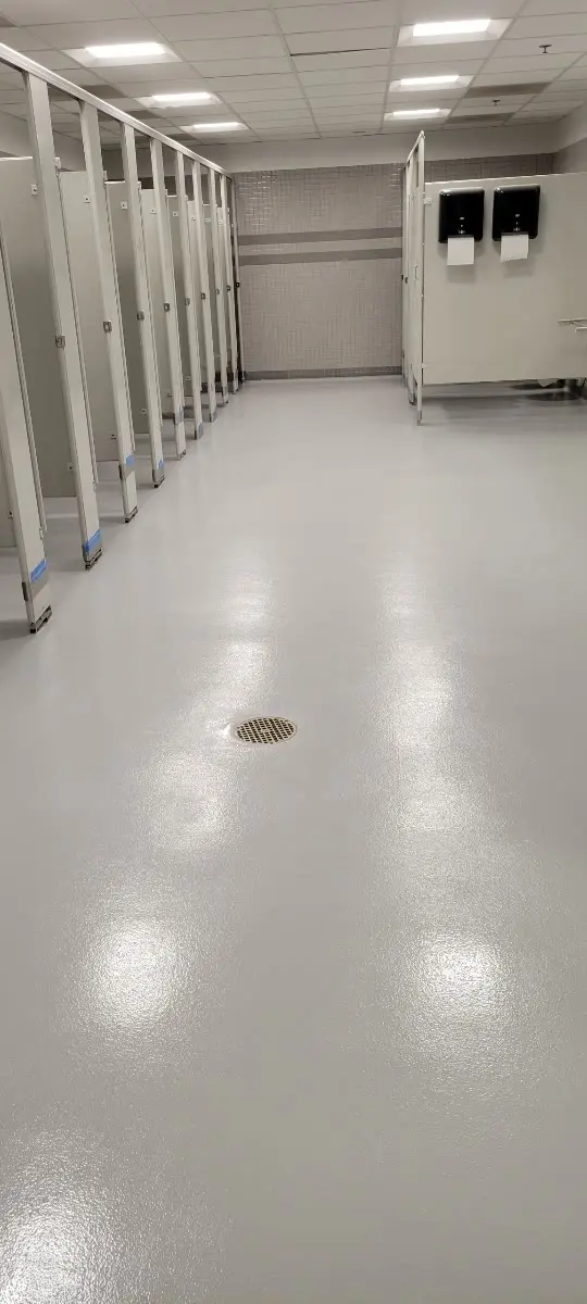 Gray broadcast epoxy floor with floor drain in a commercial restroom by Core Floorings Inc