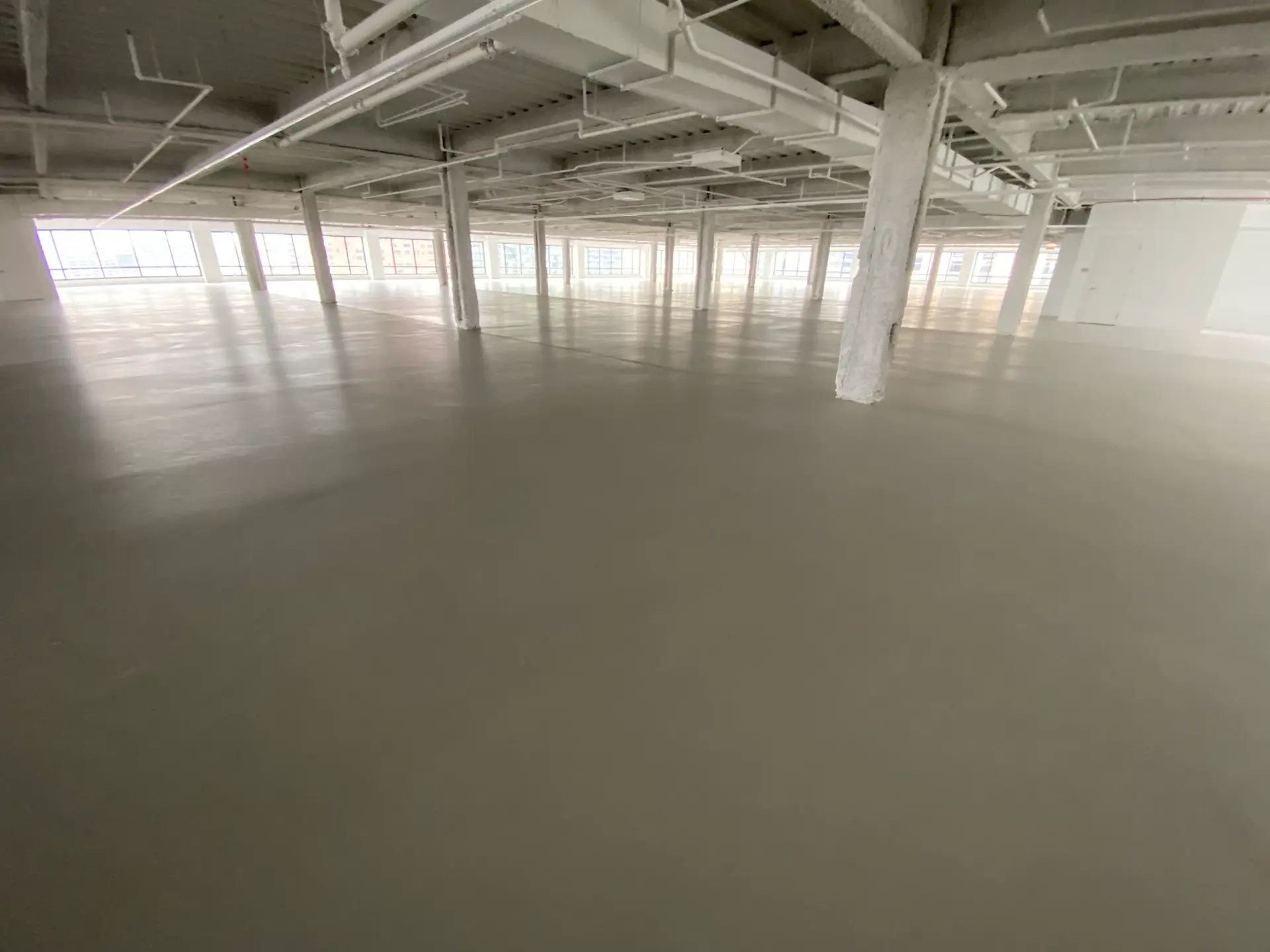 Freshly leveled cementitious underlayment across an open commercial floor with painted columns by Core Floorings Inc
