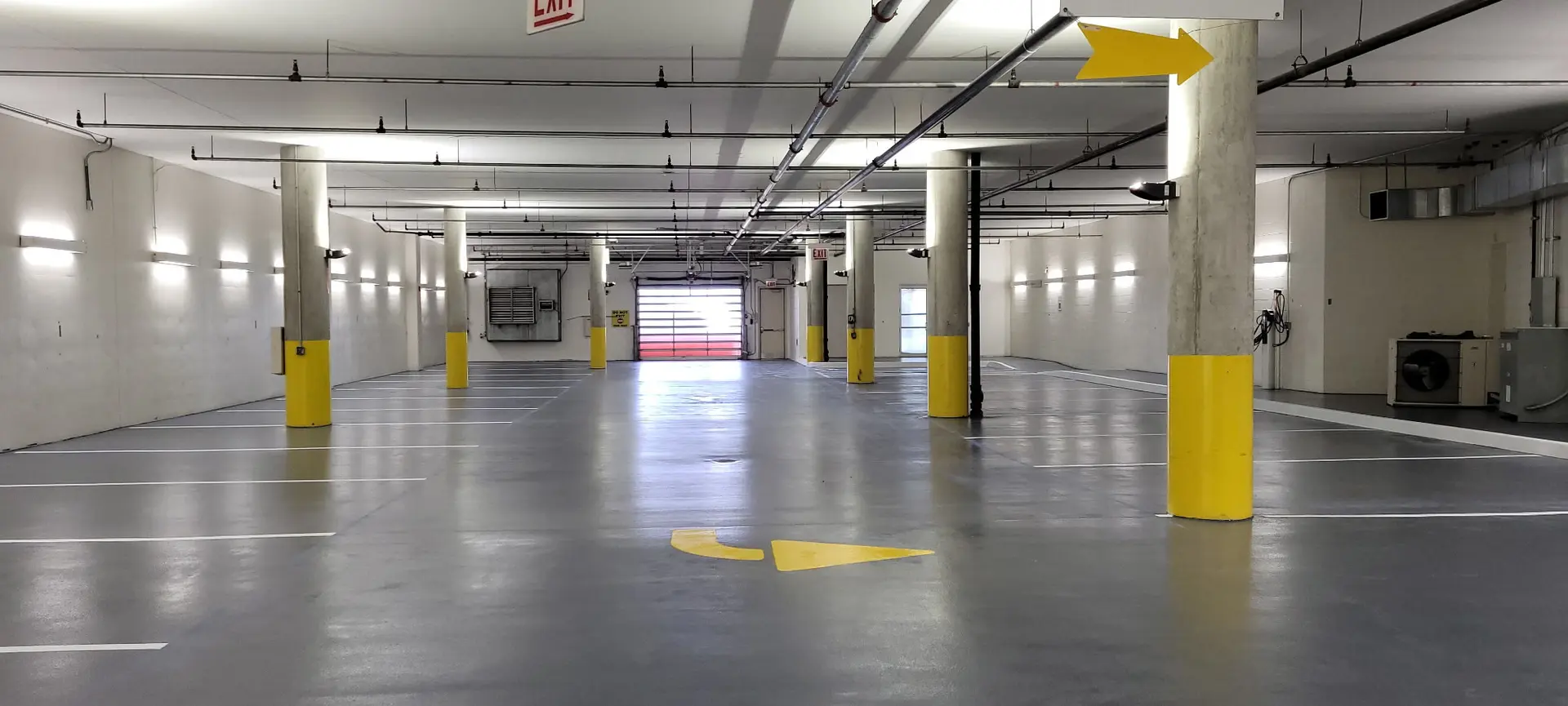 Gray traffic coating with painted stall lines and yellow column guards in a parking garage by Core Floorings Inc