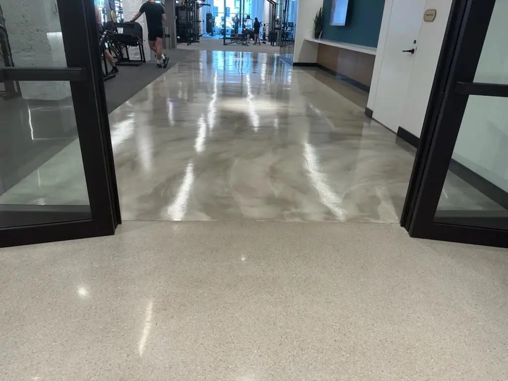 Metallic marbled troweled topping beside polished concrete at a fitness center entrance by Core Floorings Inc